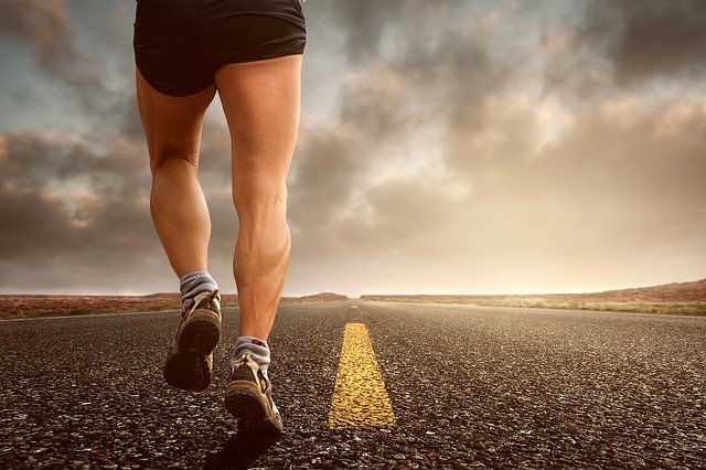 A person running on an asphalt road, framed only from the waist down.