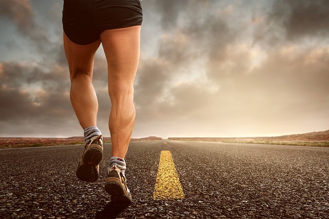A person running on a road, facing away from the camera, waist down in the frama, against a flat, desertic horizon.